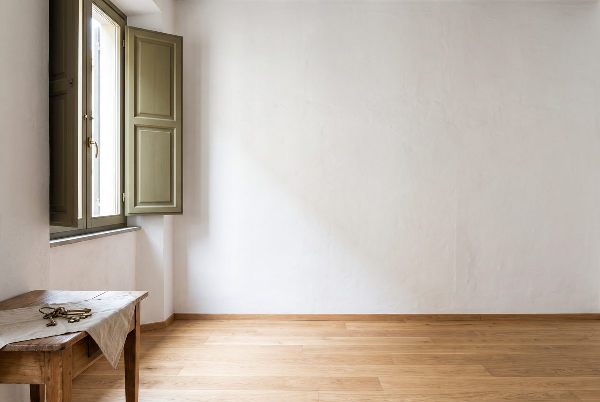 Stanza vuota e luminosa con parquet chiaro e persiane verde oliva aperte, un mazzo di chiavi su un tavolino di legno