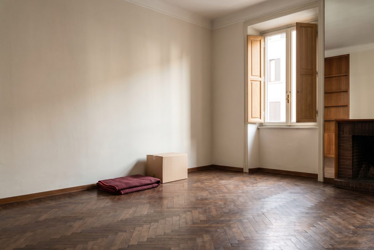 Stanza vuota di un appartamento con parquet a spina, persiane di legno naturale e una scatola di cartone lasciata in un angolo