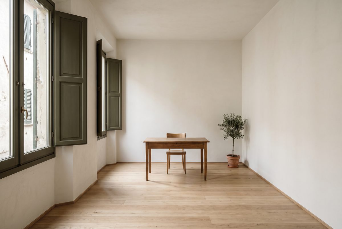 Ufficio vuoto e luminoso con finestre alte, pavimento in legno chiaro e persiane verde oliva