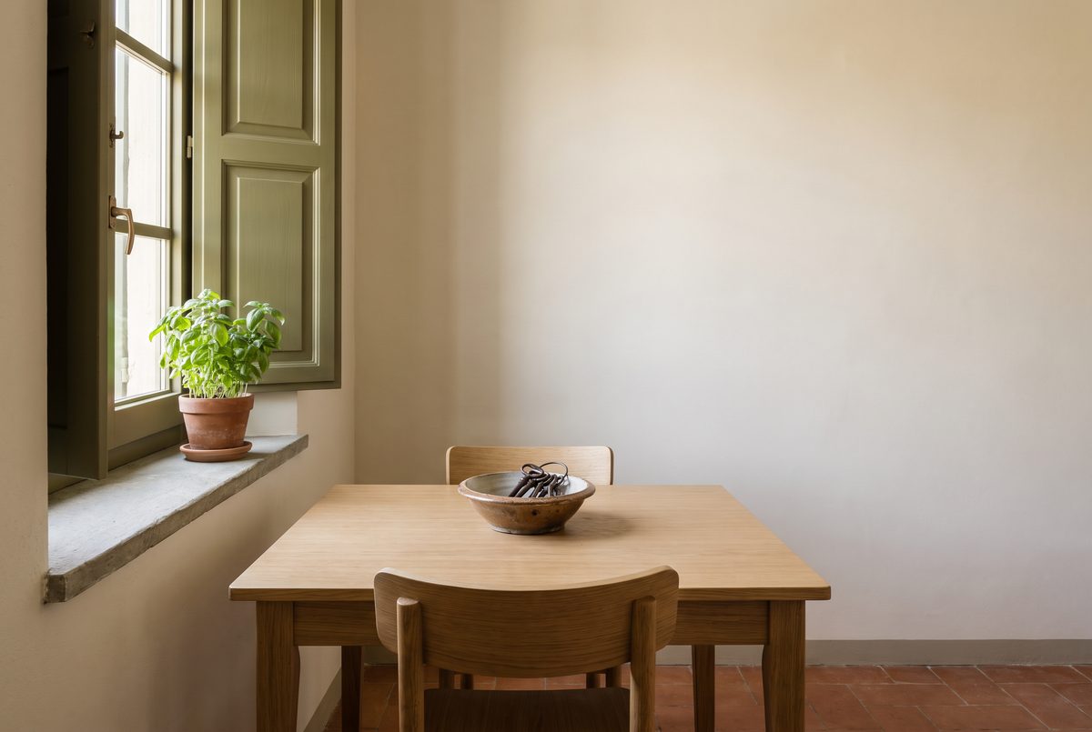 Cucina arredata e in ordine con tavolo di legno chiaro, un mazzo di chiavi in una ciotola di ceramica e una pianta di basilico sul davanzale
