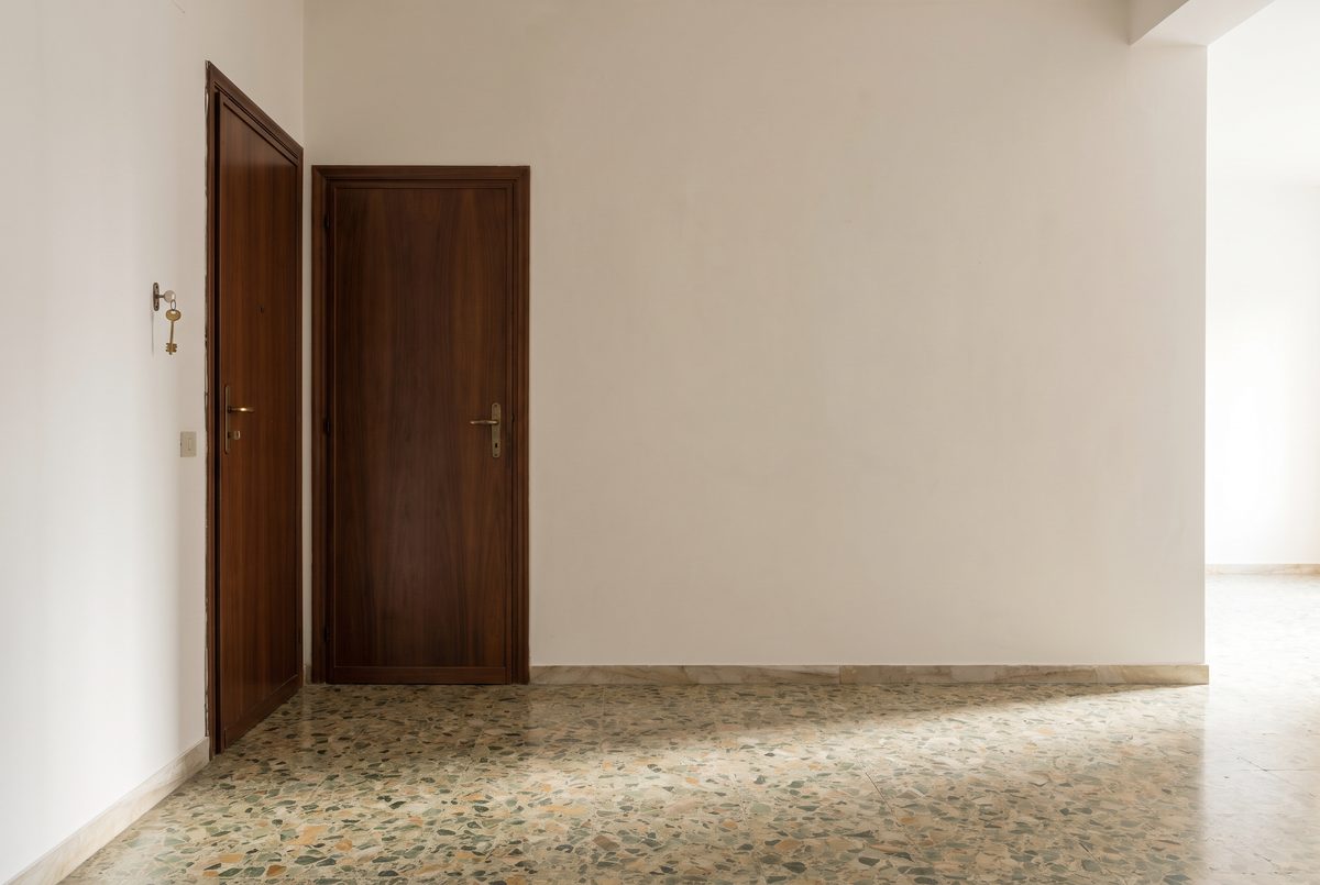Ingresso vuoto di un appartamento con pavimento in graniglia e porta di legno chiusa