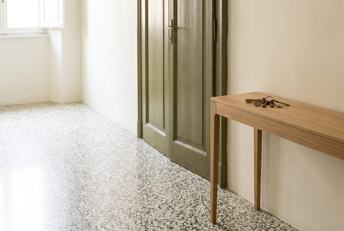 Ingresso luminoso di un appartamento con pavimento in graniglia e un mazzo di chiavi su una consolle di legno