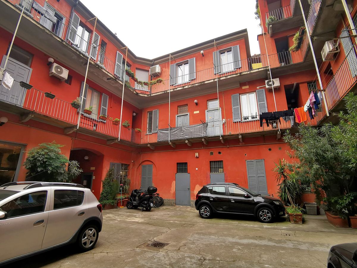 Una casa di ringhiera rossa in viale Monza, a Milano, con i negozi al piano terra